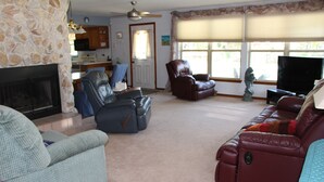 Ein Wohnzimmer mit Kamin, Ledersofas, Fernseher und einer Küche im Hintergrund.