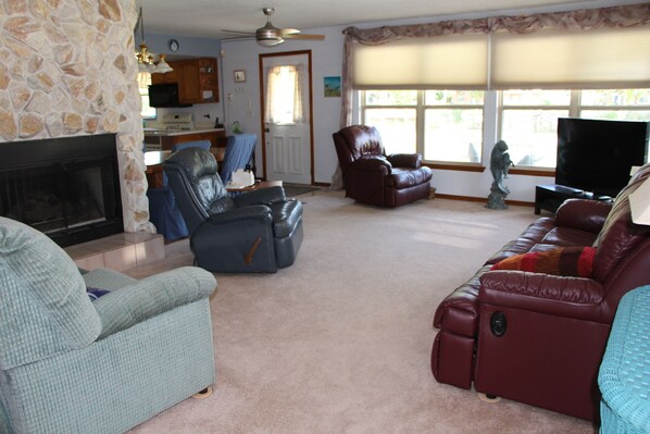 A living room with a fireplace, leather sofas, a television, and a kitchen in the background.