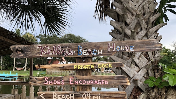 Ein hölzernes Wegweiser mit Hinweisen zu 'Celle's Beach House', 'Privater Steg', 'Badeschuhe erwünscht', 'Strand 0,6 km' und 'Aussichtspunkt 0,2 km'.