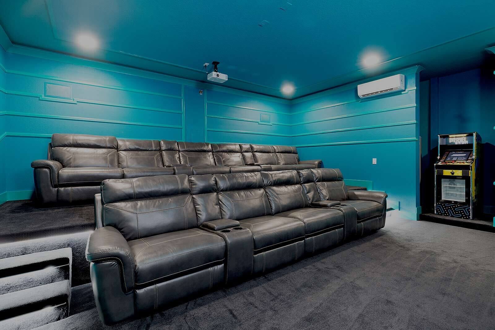 Een thuisbioscoopruimte met twee zwarte leren fauteuils, een aan het plafond gemonteerde projector en een gameconsole.