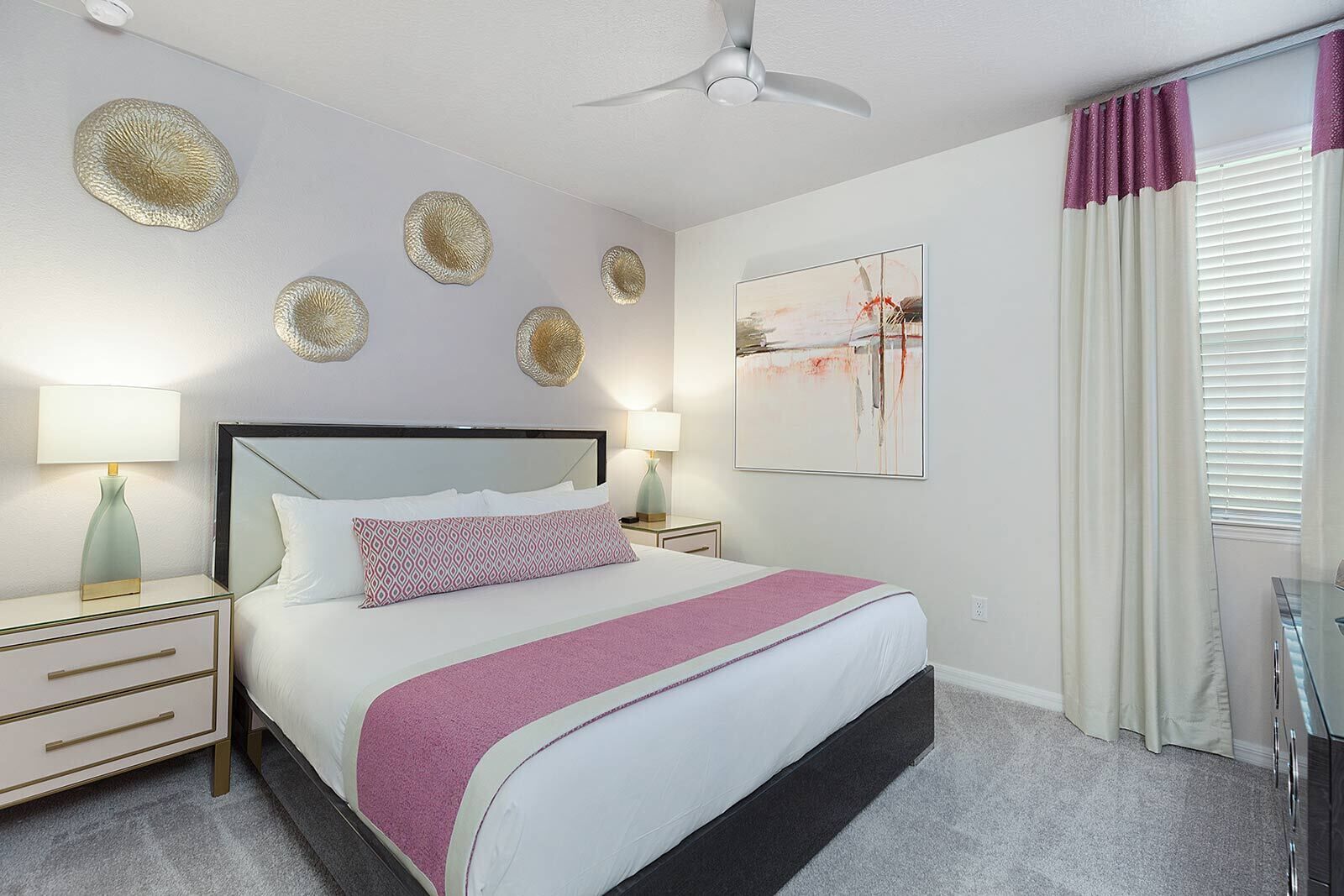 A modern bedroom with a large bed, two bedside tables, a ceiling fan, decorative wall art, and a window with curtains.