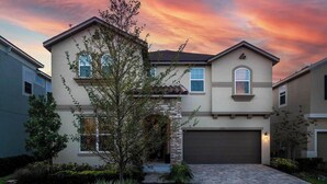 A two-story house with a stone facade, a garage, and a well-maintained front yard with a tree and shrubs. - Feature-Rich Home Near Disney w Treehouse & Superhero BRs, Theater, Arcade, & Ga (Kissimmee)