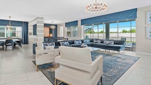 A spacious living room with a large sectional sofa, a dining area with a glass table, and a kitchen in the background. - Stellar Home w/ Space & Toy Themed BRs, Theater, Arcade & Pool - Near Top Parks (Kissimmee)