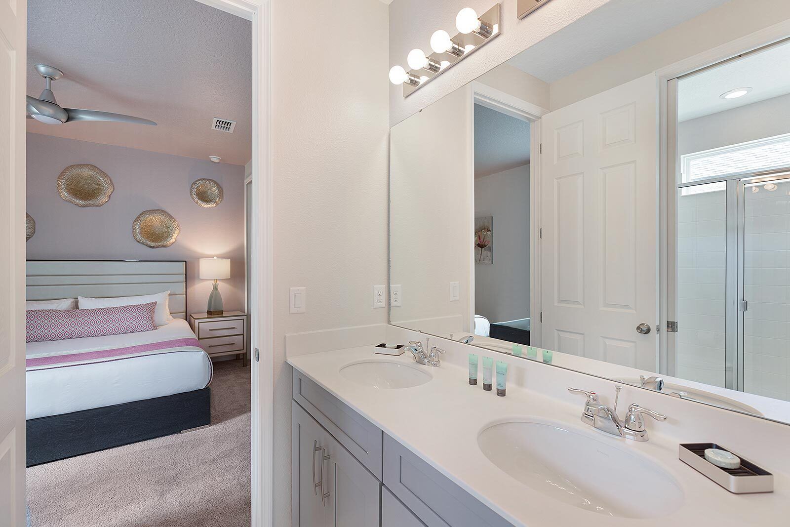 A modern bathroom with two sinks, a large mirror, and a ceiling fan.