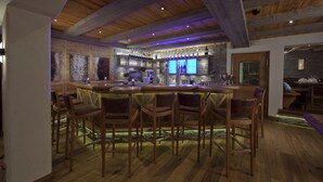 A bar area with wooden chairs and a bar counter, featuring a stone wall and wooden ceiling beams. - Landhotel Vordergrub (Kitzbuhel)