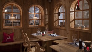 A wooden interior with arched windows, a wooden table set for dining, and a bench with a red pillow. - Landhotel Vordergrub (Kitzbuhel)