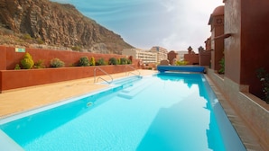 A swimming pool with a clear blue water, surrounded by a red wall and a mountain in the background. - Playa - Tamanca 1.3 SEA VIEW AND CLOSE TO THE BEACH (Arona)