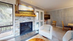 A living room with a stone fireplace, a large window, and a view of the outdoors.
