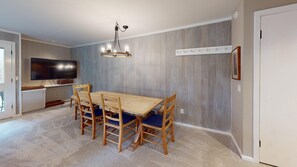 A dining area with a wooden table and chairs, a chandelier, a flat-screen TV, and a coat rack. - Cottonwood Condo 1413 - Near Ice Rink 3BR Condo in Sun Valley (Sun Valley)