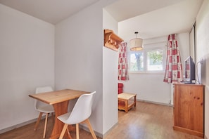 A room with a wooden table and chairs, a small red sofa, a wooden cabinet, and a window with patterned curtains. - Studio abordable à 150m des remontées | Piscine (Les Deux Alpes)