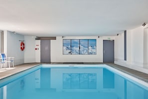 An indoor swimming pool with a view of snowy mountains through a large window.
