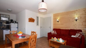 Un espace de vie compact comprenant une table à manger en bois, un canapé rouge, un coin cuisine équipé d’appareils électroménagers et un mur en bois agrémenté de luminaires fixés au mur.