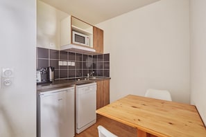 A compact kitchenette with a microwave, a coffee maker, a dishwasher, and a wooden table. - Studio abordable à 150m des remontées | Piscine (Les Deux Alpes)