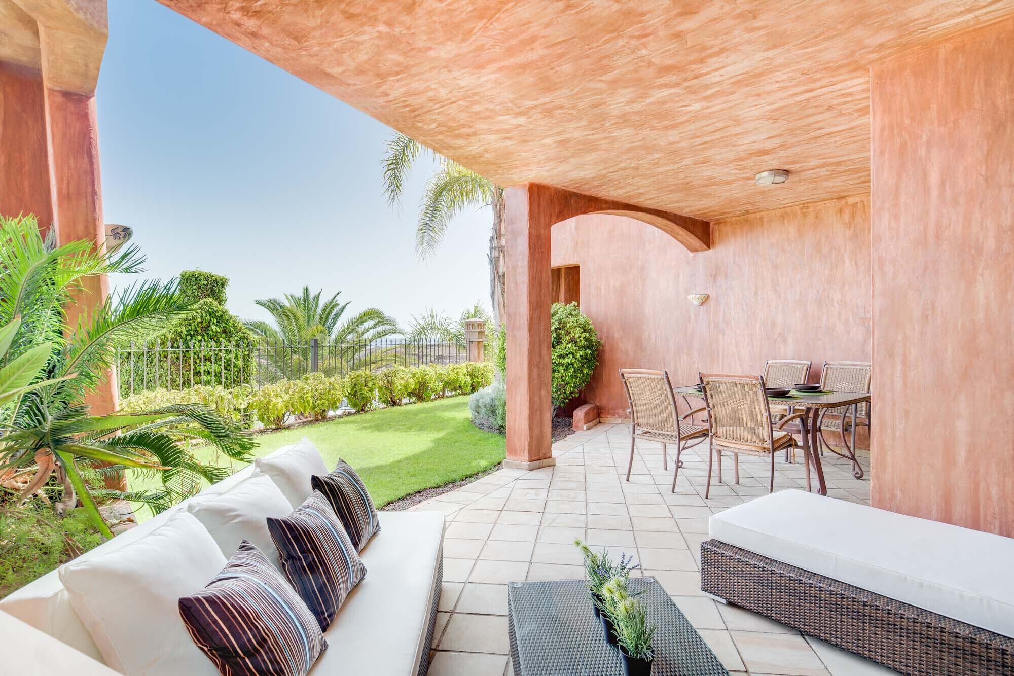 A covered outdoor seating area with a sofa and chairs, a small table, and a potted plant.