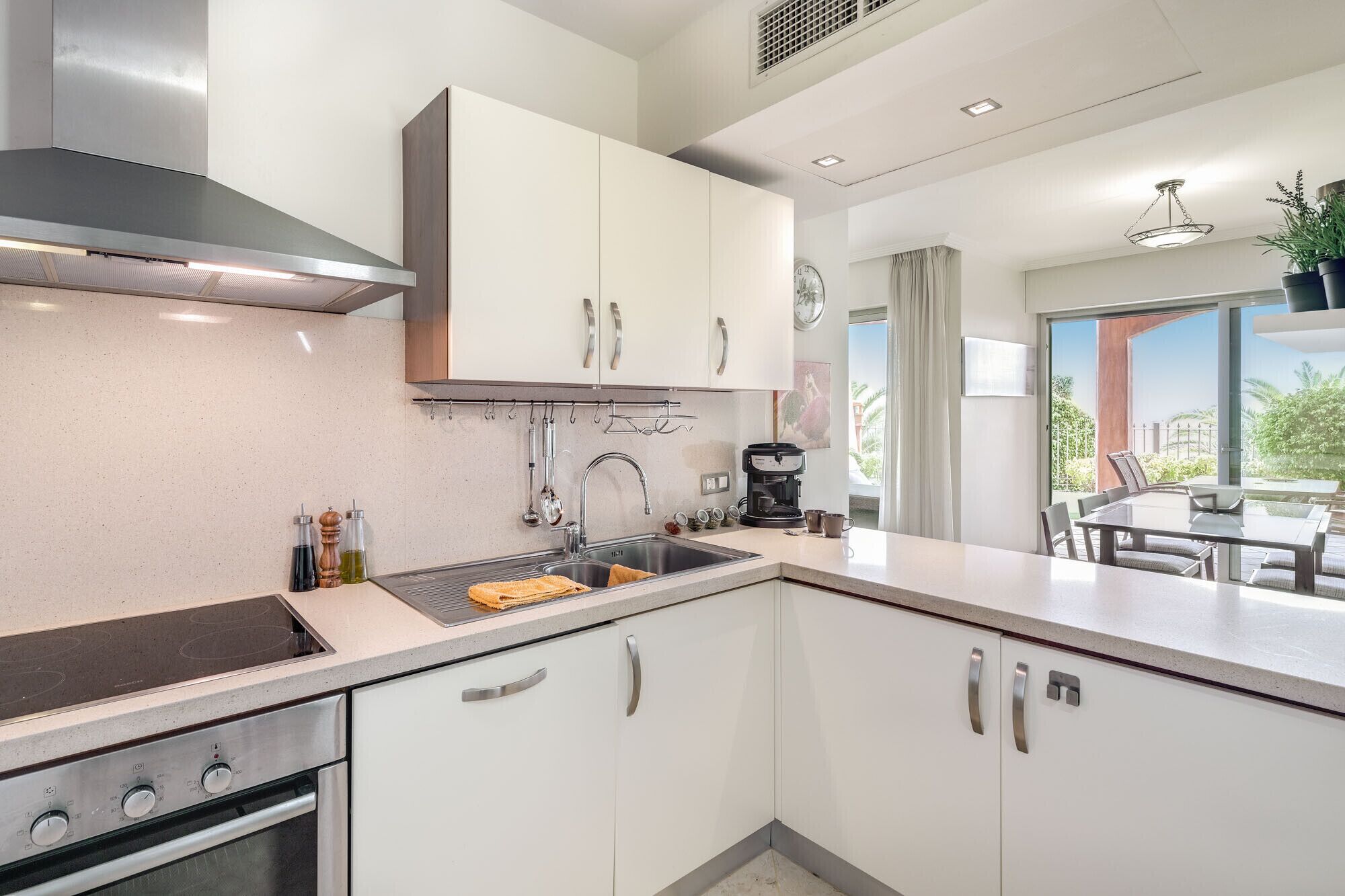 A modern kitchen with white cabinets, stainless steel appliances, and a dining area with a view.