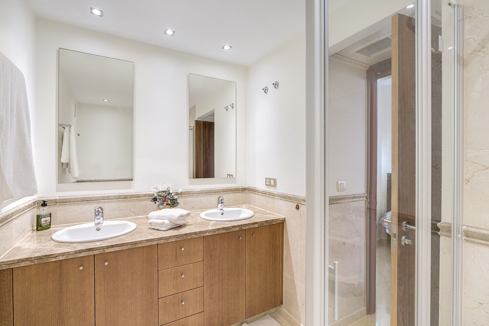 Une salle de bain moderne avec deux vasques, des meubles en bois, un grand miroir et une cabine de douche en verre.