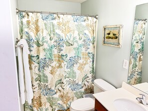 Baño con cortina de ducha con estampado de arrecife de coral, inodoro, lavamanos con espejo y un cuadro en la pared.
