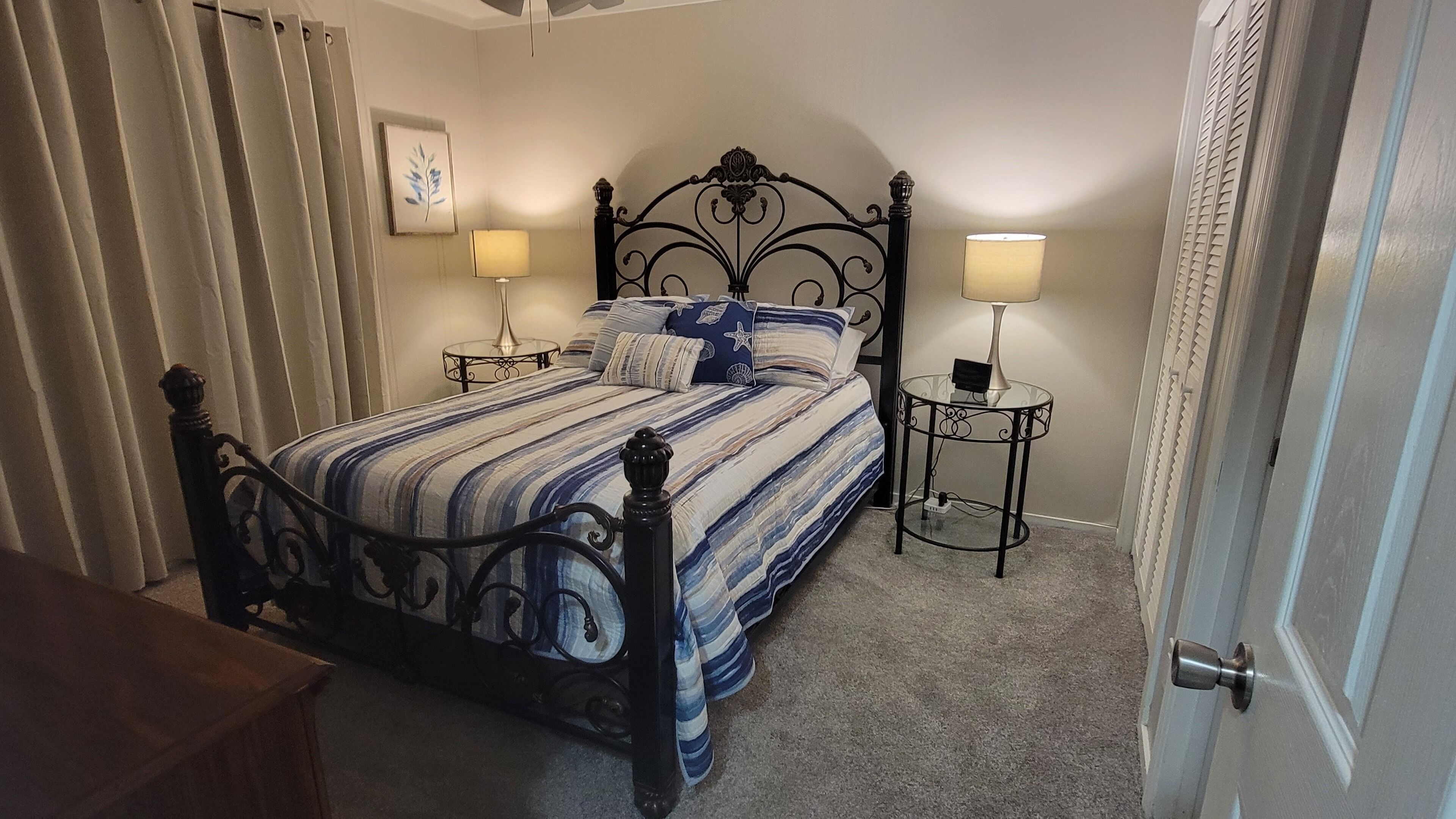 A bedroom with a bed, two bedside tables, a lamp on each table, a door, and a window with curtains.