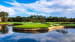 Un parcours de golf agrémenté d’un plan d’eau, entouré d’arbres et offrant une vue sur un ciel dégagé.
