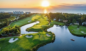 A golf course with water hazards, a boat, and buildings in the background.
