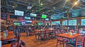 Un restaurant doté de nombreuses tables et chaises, de téléviseurs fixés aux murs et d’un bar où sont exposés divers produits.