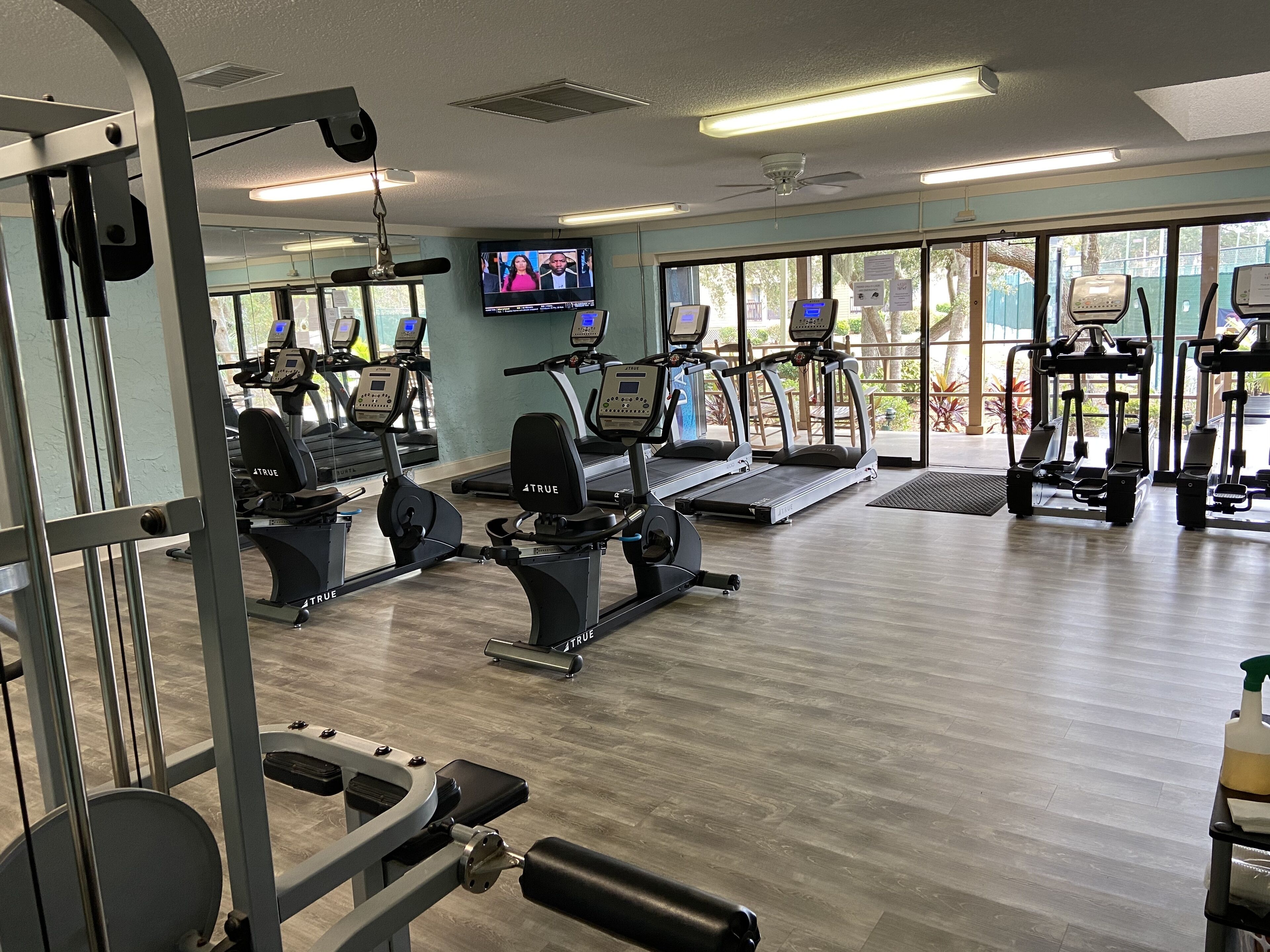A gym with cardio equipment, weight machines, and a TV screen.