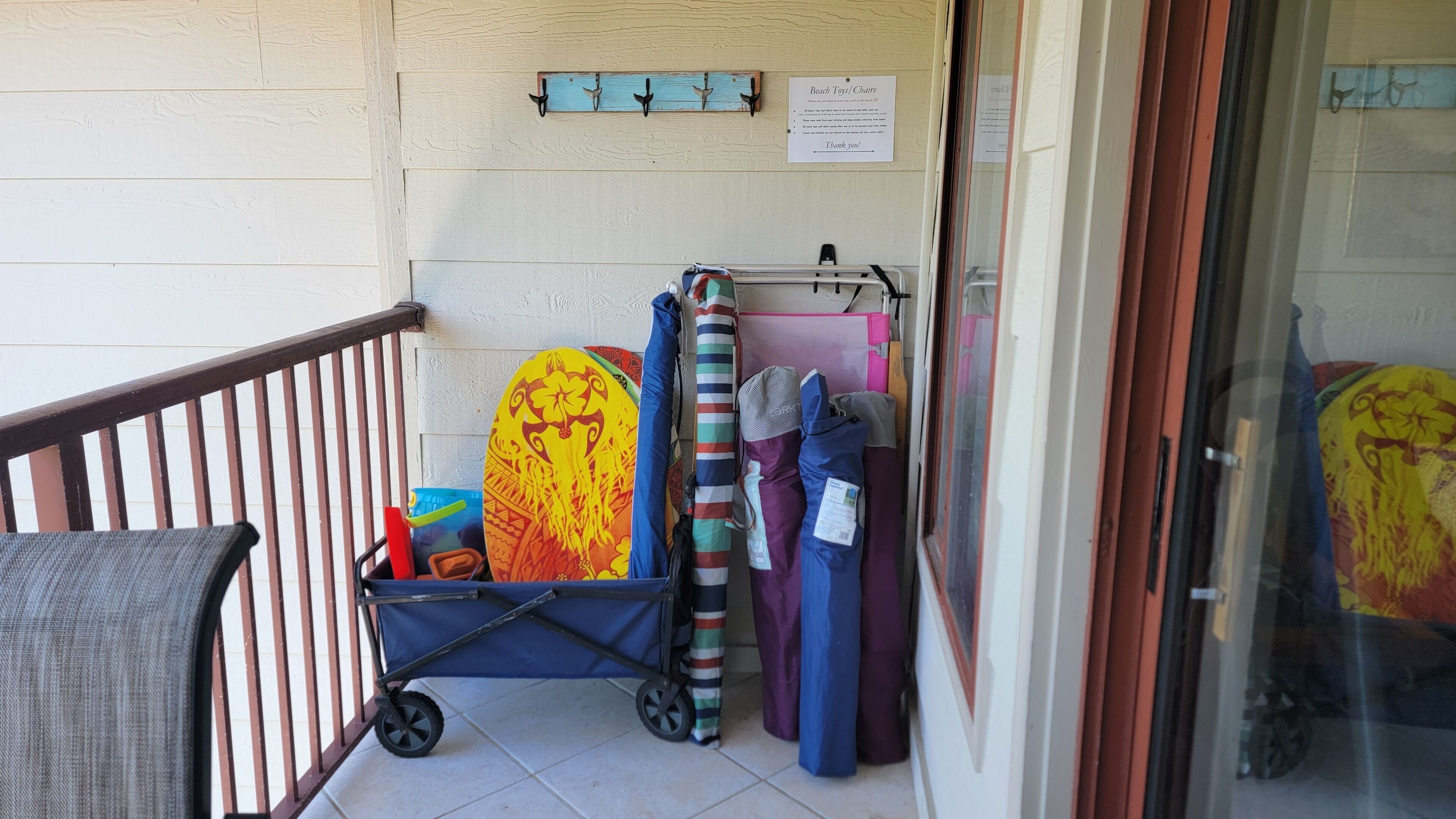 Un balcone con una sedia, un carrello con asciugamani da spiaggia colorati e un cartello appeso al muro.