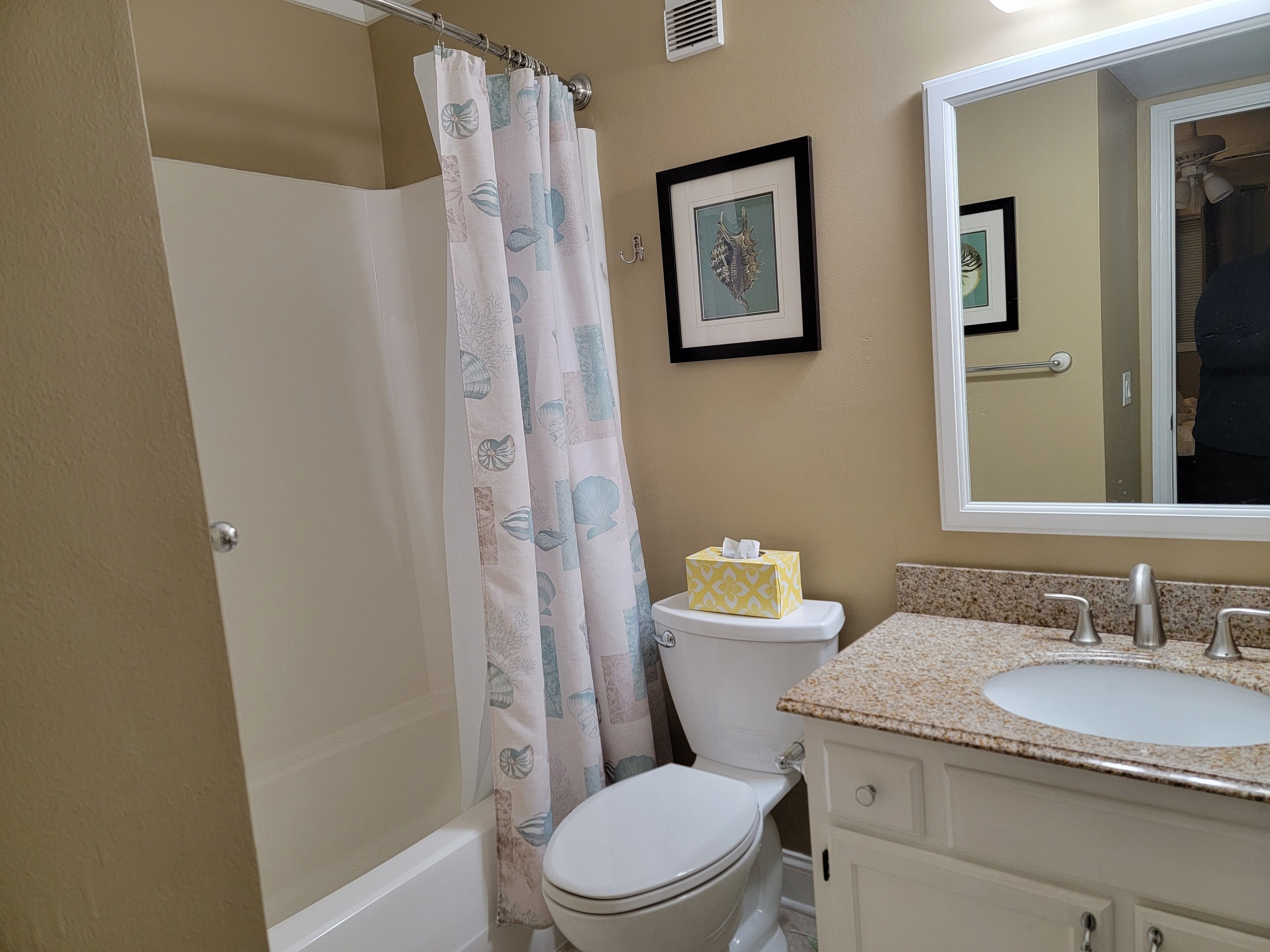 A bathroom with a shower curtain, toilet, sink, and a framed picture on the wall.