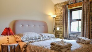 A bedroom with a bed, a lamp, a table, a window with curtains, and a stone wall. - 3 bedroom accommodation in Pontyates, near Kidwelly (Pontyates, near Kidwelly)