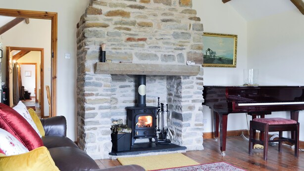 A stone fireplace with a modern stove, a grand piano, and a cozy seating area with a sofa and armchairs. - 3 bedroom accommodation in Pontyates, near Kidwelly (Pontyates, near Kidwelly)