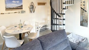 Una sala de estar moderna con una escalera espiral, un comedor con una mesa redonda y una zona de estar acogedora con una cama para mascotas.