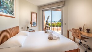 Ein Hotelzimmer mit Bett, Schreibtisch, Stuhl, einem großen Fenster mit Blick und einem Bild an der Wand.