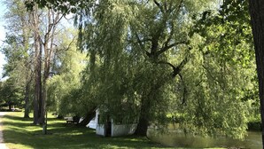 Een vredig park met een grote wilg, een klein tuinhuis en een rustig waterlichaam.