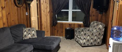 Una habitación acogedora con un sofá modular, un sillón estampado, una mesita auxiliar, un televisor y un dispensador de agua.