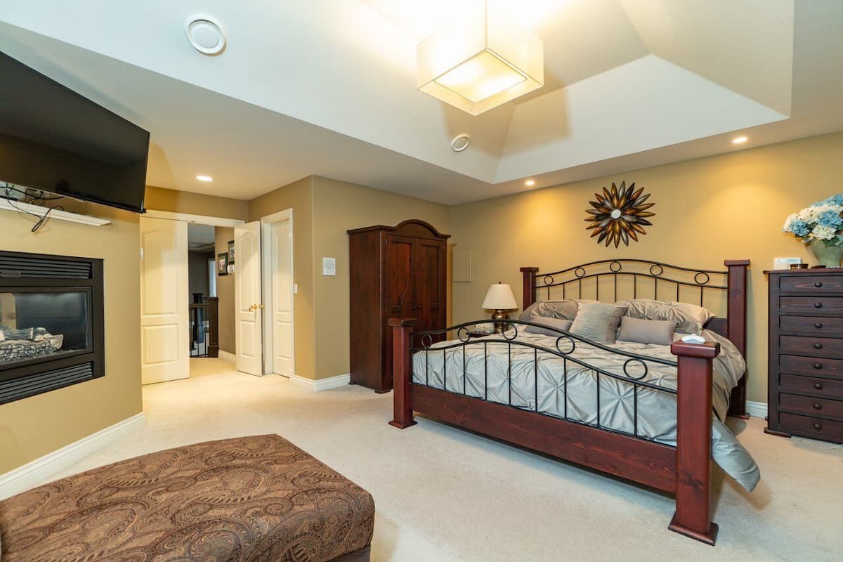 A bedroom with a bed, a nightstand, a dresser, a wall-mounted TV, and a ceiling light.