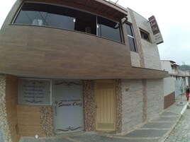 Un edificio de dos pisos con un letrero que dice 'HOTEL Pousada Santa Cruz' y servicios que incluyen TV, aire acondicionado, estacionamiento y un ambiente familiar.