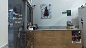 A reception area with a wooden counter, a marble wall decoration, and a sign indicating the location of the Maxa Lotação. - Hotel e Pousada Santa Cruz (Aparecida)