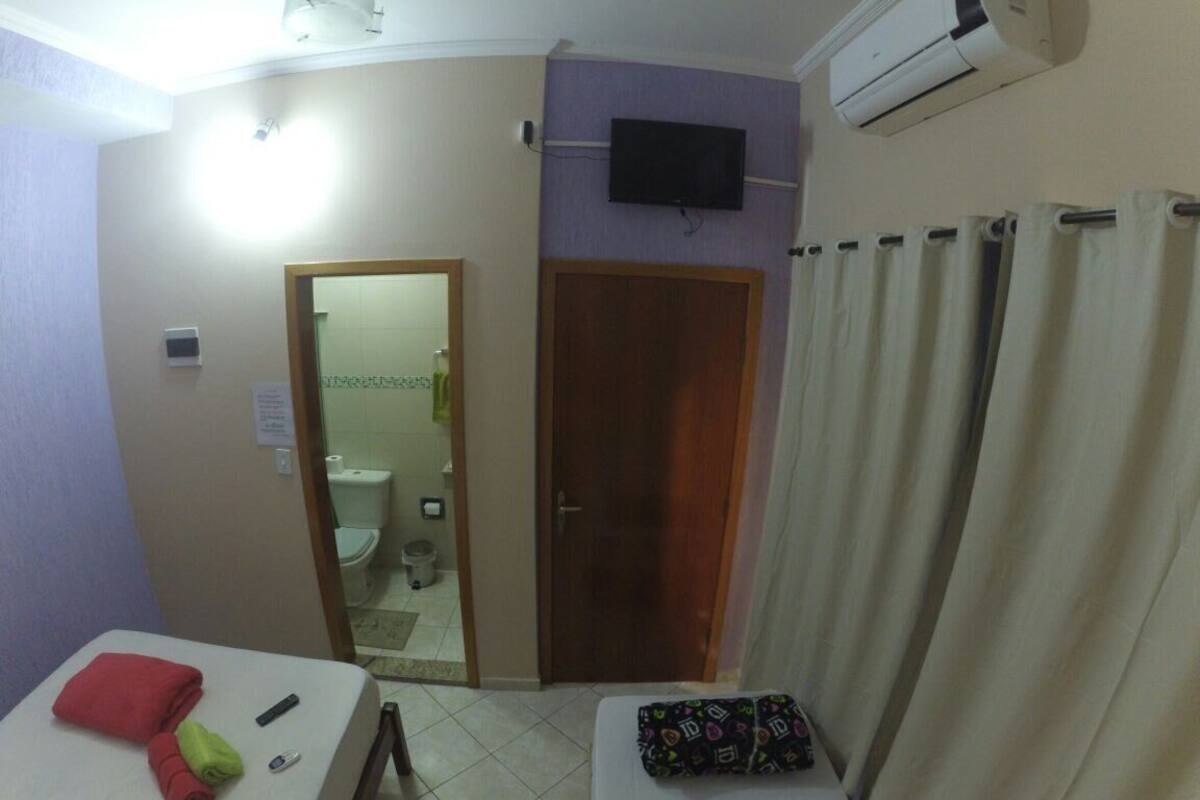 Une chambre d’hôtel avec deux lits, une télévision, la climatisation, une salle de bain avec des toilettes et un rideau de douche.