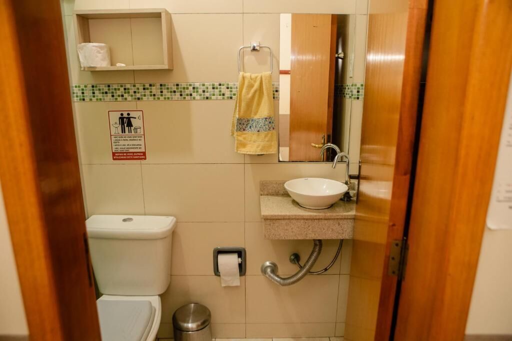 Un baño pequeño con inodoro, lavamanos y espejo. Hay una toalla colgada en la pared y un cubo de basura.