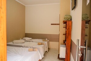 Habitación de hotel con dos camas, un estante de madera con toallas dobladas, un espejo y un pequeño electrodoméstico blanco.
