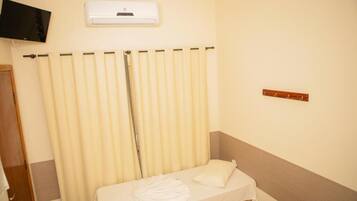 A hotel room with a bed, a TV mounted on the wall, and a window with curtains.