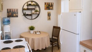 A kitchen with a round table, a chair, a water dispenser, a refrigerator, and wall art. - Patio + BBQ + Downtown Access | Paso Robles | Vine Street Guest House (Paso Robles)