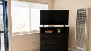 A room with a black TV stand, a window, and a wall-mounted air vent. - Patio + BBQ + Downtown Access | Paso Robles | Vine Street Guest House (Paso Robles)