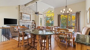 A spacious living area with a high ceiling, a fireplace, a dining table with chairs, and a large window with a view of trees. - Grand Hyatt|Creekside, multi level condo w/close access to chair 20 and views of Gore Creek (Vail)