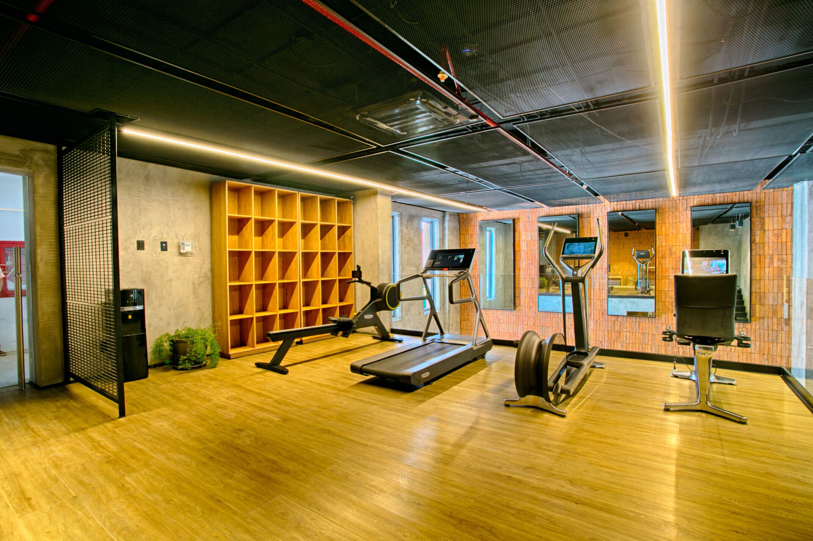 A modern gym with wooden flooring, exercise equipment, and a brick wall.