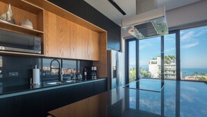 A modern kitchen with a black countertop, wooden cabinets, and a view of the ocean through large windows. - Sail View,Spacious Condo Romantic Zone Ocean Views (Puerto Vallarta)
