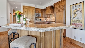 A kitchen with wooden cabinets, a granite countertop, and a bar area with a vase of flowers. - Ski-in Ski-out | Luxury | Chefs Kitchen | Garage (Park City)