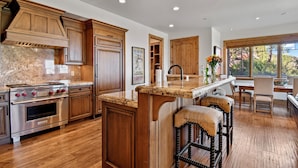 A kitchen with wooden cabinets, a built-in stove, and a large island with bar stools. - Ski-in Ski-out | Luxury | Chefs Kitchen | Garage (Park City)