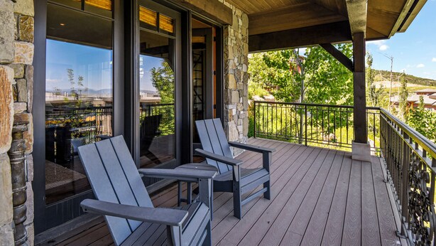 A wooden deck with Adirondack chairs, stone walls, and a view of a mountainous landscape. - Ski-in Ski-out | Luxury | Chefs Kitchen | Garage (Park City)