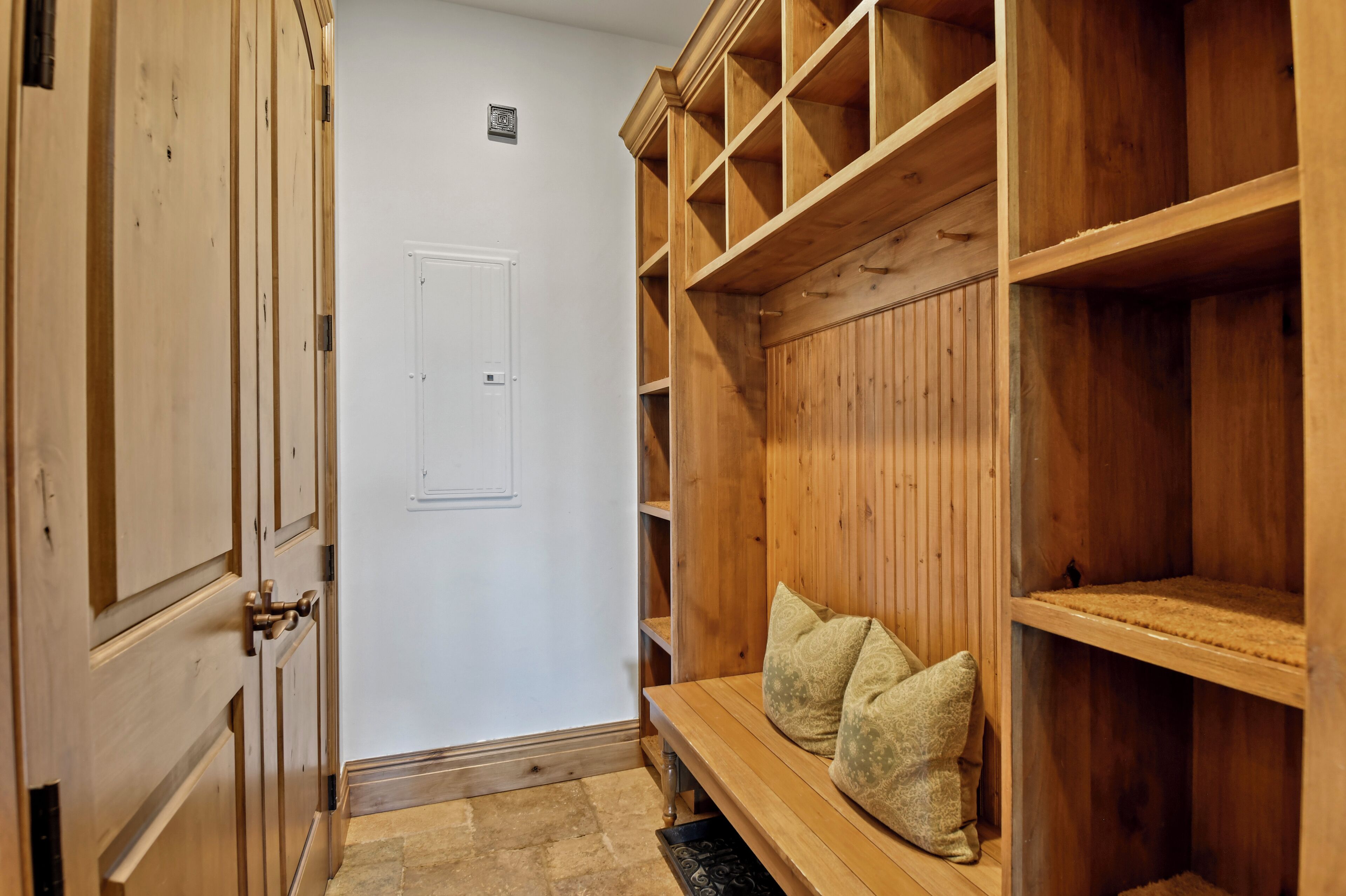 A hallway with wooden paneling, a bench with cushions, and a white door.